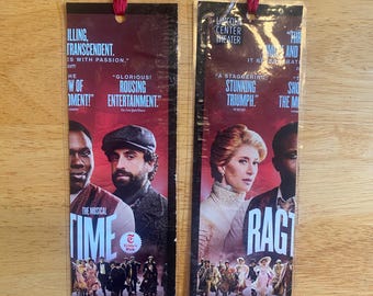 May include: Two rectangular paper bookmarks featuring promotional imagery for the musical Ragtime at Lincoln Center Theater. Each bookmark has a red yarn tassel at the top and displays cast portraits, production titles, and critical review quotes.