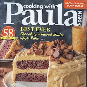 May include: A magazine cover featuring a chocolate and peanut butter layer cake with a slice removed. The magazine is titled "Cooking with Paula Deen" and the cover features the text "Best-Ever Chocolate + Peanut Butter Layer Cake".