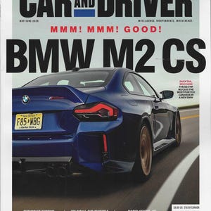 Puede incluir: La portada de la revista Car and Driver presenta un coche deportivo azul BMW M2 CS. El título de la revista está en letras negras grandes, con la fecha de publicación y otro texto visible. El coche tiene una matrícula de Nueva Jersey.