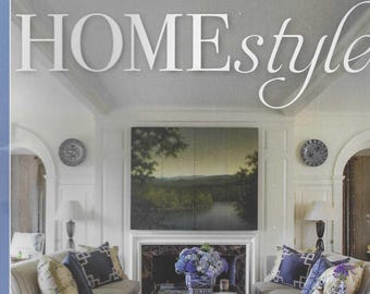 May include: The cover of a "HOMEstyle" magazine features a living room with two sofas, a coffee table, and a fireplace. The text "55+ tips for LAVISH Interiors" is displayed. The room is decorated with blue and white accents, and a landscape painting hangs above the fireplace.