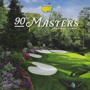 以下が含まれることがあります： 90th Masters Tournament Journal の表紙には、緑のフェアウェイ、白い砂のバンカー、色とりどりのツツジが描かれたゴルフコースが写っています。「90th Masters」と「April 6-12, 2026」の文字が含まれています。オーガスタ・ナショナル・ゴルフクラブの画像です。