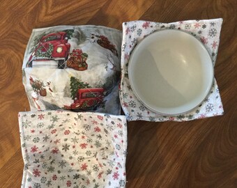 May include: Set of three quilted pot holders featuring a winter holiday theme. The pot holders are made of a white fabric with a red truck, a Christmas tree, and snowflakes. The pot holders are perfect for protecting your hands from hot dishes.