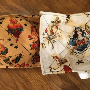 May include: Two fabric pot holders with a nautical theme. One is beige with a skull, dagger, heart, and stars. The other is white with an anchor, mermaid, and the text "Sink or Swim".