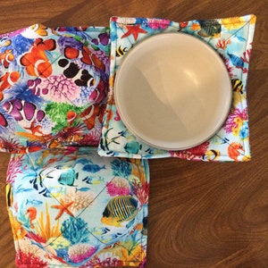 May include: Three colorful bowl cozies with a sea life pattern. The cozies are made of fabric and have a quilted design. The cozies are in a variety of colors, including blue, green, orange, and yellow. The cozies are perfect for protecting your bowls from heat.