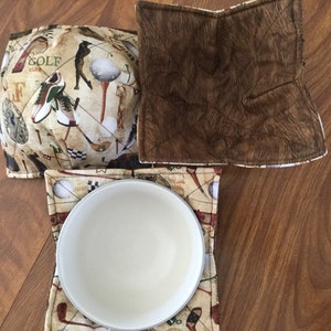 May include: Set of three golf-themed quilted pot holders. The pot holders are brown and beige with a golf club, golf ball, and golf shoe pattern. The text "GOLF CLUB" is visible on one of the pot holders.