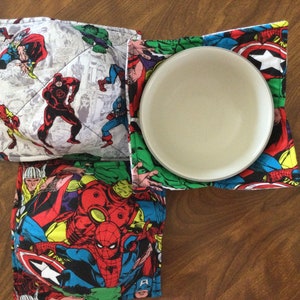 Puede incluir: Tres agarraderas acolchadas con un tema de superhéroes de cómics. Las agarraderas presentan una variedad de superhéroes, incluyendo Spider-Man, Iron Man, Captain America y Hulk. Las agarraderas están hechas de una tela suave acolchada y son perfectas para proteger tus manos de los platos calientes.