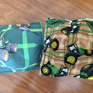 May include: Two square bowl cozies. One is green with a tractor design and a plaid pattern. The other is tan with a green and brown plaid pattern and a tractor design. Both are quilted.