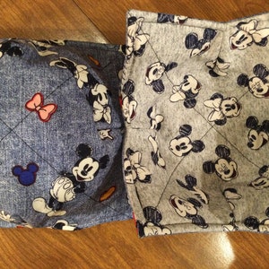 May include: Two reversible pot holders with a blue denim fabric on one side and a gray fabric on the other side. Both sides feature a repeating pattern of Mickey Mouse and Minnie Mouse.