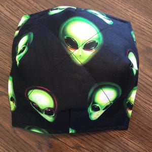 Könnte beinhalten: Schwarze Stoffmaske mit einem sich wiederholenden Muster aus grünen Alien-Gesichtern.