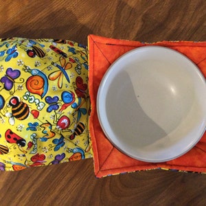 Könnte beinhalten: Zwei gesteppte Schalenuntersetzer. Einer ist gelb mit einem bunten Käfermuster, einschließlich Bienen, Schmetterlingen und Marienkäfern. Der andere ist orange und hält eine weiße Keramikschale. Das Wort "BUGS" ist sichtbar.