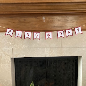 May include: A red and white banner with the words "RING DAY" and a thumbs up symbol hanging above a fireplace.