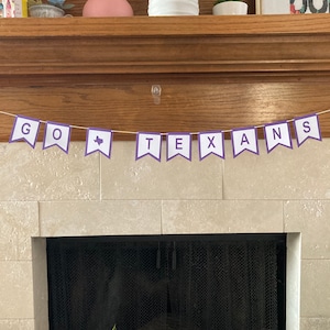 May include: A purple and white banner with the words "GO TEXANS" hanging above a fireplace. The banner has a small outline of the state of Texas on one of the flags.