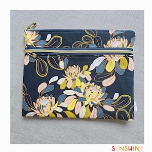 以下が含まれることがあります： 黄色、ピンク、青の花柄がプリントされた黒いジッパー付きポーチ。ポーチにはジッパーが2つ付いています。