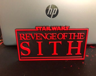 Pode incluir: Um sinal impresso em 3D preto e vermelho com o texto "STAR WARS REVENGE OF THE SITH" em letras vermelhas.
