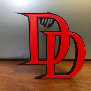 May include: A red and black 3D printed letter D, the logo for the superhero Daredevil.