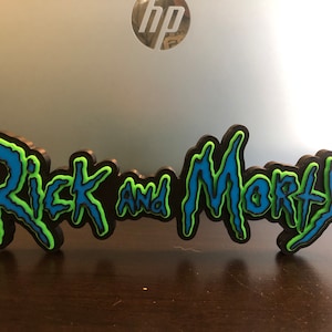 Może przedstawiać: Tr&oacute;jwymiarowa tabliczka z napisem "Rick and Morty" w niebiesko-zielonej kolorystyce. Litery są stylizowane na ząbkowane, prawie jak gdyby kapały.