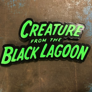 May include: Black and green sign with the text "Creature from the Black Lagoon" in a retro style font.