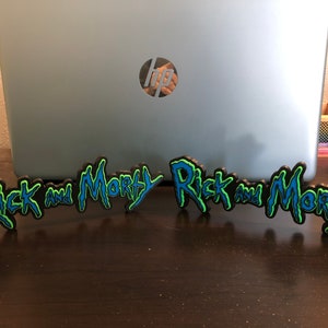 Może przedstawiać: Dwa czarne, niebieskie i zielone znaki drukowane w 3D z napisem "Rick and Morty".