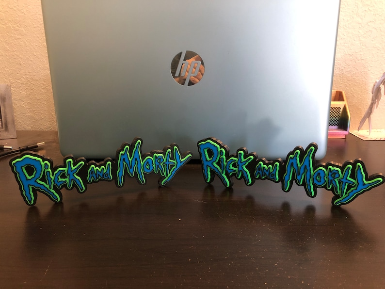 Może przedstawiać: Dwa czarne, niebieskie i zielone znaki drukowane w 3D z napisem "Rick and Morty".