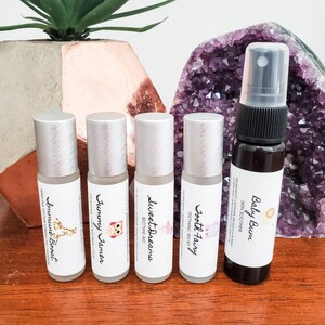 May include: Five essential oil roller bottles and a spray bottle with labels and illustrations. The bottles are silver with white labels and the spray bottle is black with a white label. The labels include the names "Baby Bum", "Tooth Fairy", "Sweet Dreams", "Yummy Tummy", and "Immune Boost".