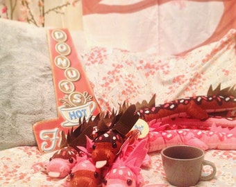 May include: Five plush pink and brown worm-like creatures with black eyes and brown spots. The worms are on a pink and white floral patterned fabric with a brown coffee cup in the background.