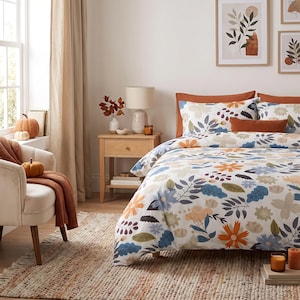 May include: A bedding set featuring a white duvet cover and pillowcases with a multi-colored floral and leaf pattern in shades of orange, blue, and green. The set includes solid orange pillow shams and a matching rectangular accent pillow.