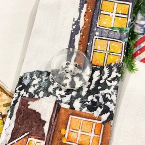 May include: A white fabric with a Christmas-themed print featuring houses with windows and snow. A clear plastic button is visible in the center of the image.