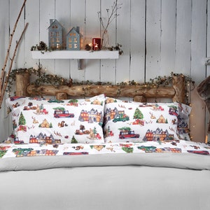 May include: A white bed with a gray duvet cover and two white pillowcases with a Christmas-themed print of red trucks, houses, and trees. The bed is decorated with a garland of lights and branches.