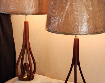 May include: Two wooden table lamps with brown shades and a unique, curved, wooden base.