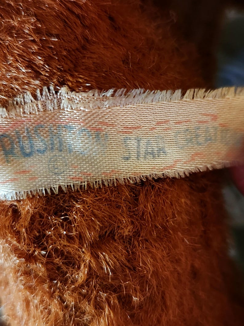 May include: Close-up of a brown plush toy with a tag that reads "PUSH STAR". The plush has long, shaggy fur. The tag is a light beige color with red and blue text.
