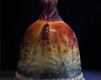 May include: A decorative glass bell with a blue top and base, transitioning to yellow, orange, and red hues. The bell features a detailed landscape design and a frieze of figures around the base. The bell is approximately 6 inches tall.