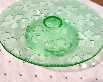 May include: A green glass serving plate with a floral pattern. The plate has a raised center and a textured surface. The floral design is repeated across the plate's surface. The plate is a vibrant shade of green.