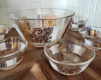 May include: A set of clear glass bowls with a decorative gold and brown floral pattern. The set includes a large serving bowl and several smaller bowls, ideal for serving salads or snacks. The bowls have a vintage aesthetic.