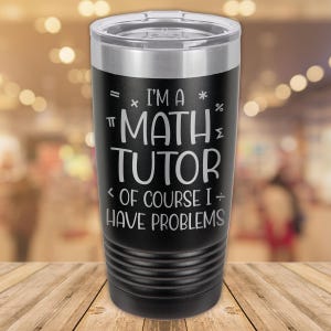 May include: Black insulated tumbler with a silver rim and lid. The tumbler features the text "I'M A MATH TUTOR OF COURSE I HAVE PROBLEMS" in white, along with mathematical symbols.