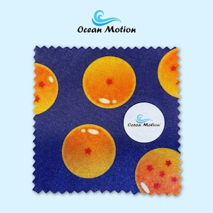 Può includere: Un tessuto quadrato con un motivo ripetuto di globi arancioni con accenti di stella rossa su uno sfondo blu scuro. Il tessuto presenta anche il testo "Ocean Motion" e un logo.