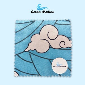 Puede incluir: Una muestra de tela cuadrada con un fondo azul claro y un diseño de nube blanca. Líneas negras crean un patrón en la tela. Las palabras "Ocean Motion" están impresas en la tela.