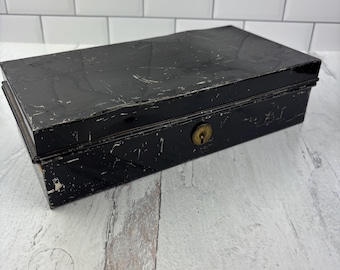 May include: A black metal box with a lock and keyhole. The box has a worn, distressed finish and appears to be vintage.
