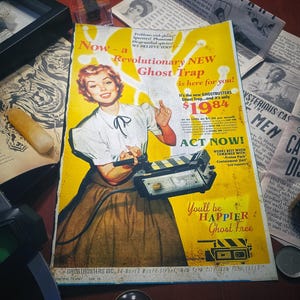 May include: A vintage advertisement for a "Revolutionary NEW Ghost Trap" featuring a woman in a yellow dress holding a device. The ad is yellow with black text and the price is $19.84. The text reads "Now a Revolutionary NEW Ghost Trap is here for you! It's the new GHOSTBUSTERS Ghost Trap, and it's only $19.84. ACT NOW!"