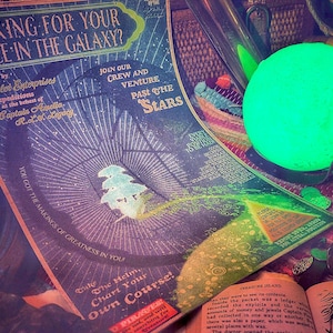 Puede incluir: Un p&oacute;ster vintage con un dise&ntilde;o de galaxia y el texto "Looking for your place in the galaxy?" El p&oacute;ster est&aacute; rodeado de varios objetos, incluyendo un orbe verde brillante, un libro y una caja de madera.