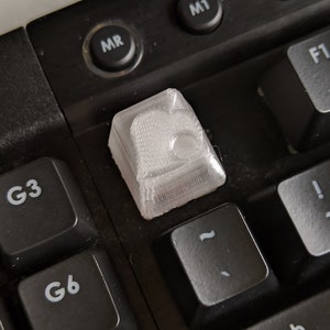 May include: A clear, 3D-printed keycap sits on a black keyboard. The keycap is textured and has a unique design. Other black keys with white lettering are visible, including function keys and keys labeled "G3", "G6", and "G9".