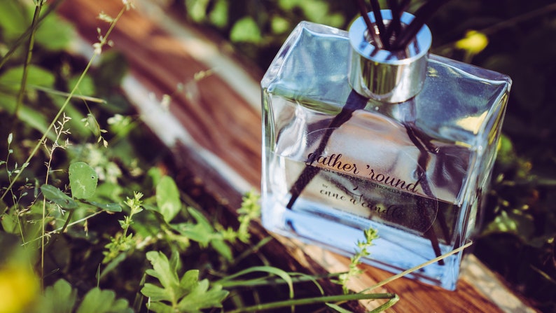 May include: A clear glass bottle with a silver cap and black diffuser sticks. The bottle is labeled "gather 'round come a'round".