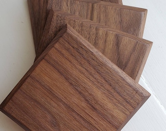 May include: Four square wooden coasters made of walnut wood. The coasters are stacked on top of each other.
