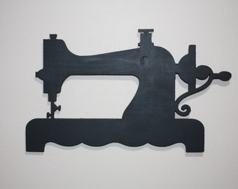 May include: A black silhouette of a vintage sewing machine, cut out of wood and mounted on a white wall.