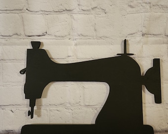 May include: Black silhouette of a vintage sewing machine, standing on a wooden surface.