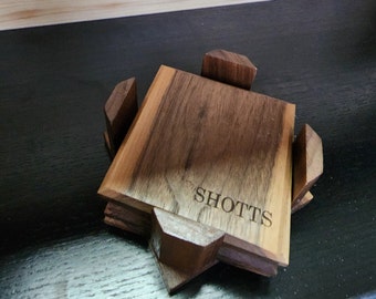 May include: A wooden coaster set with four pieces, each with a beveled edge. The top piece has the name "Shotts" engraved on it.