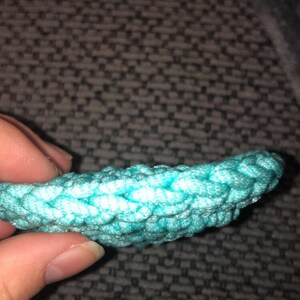 May include: Close-up of a turquoise crocheted item, possibly a decorative element or part of a larger craft project. The texture is clearly visible, with a tight, woven pattern. The color is a bright, vibrant turquoise.