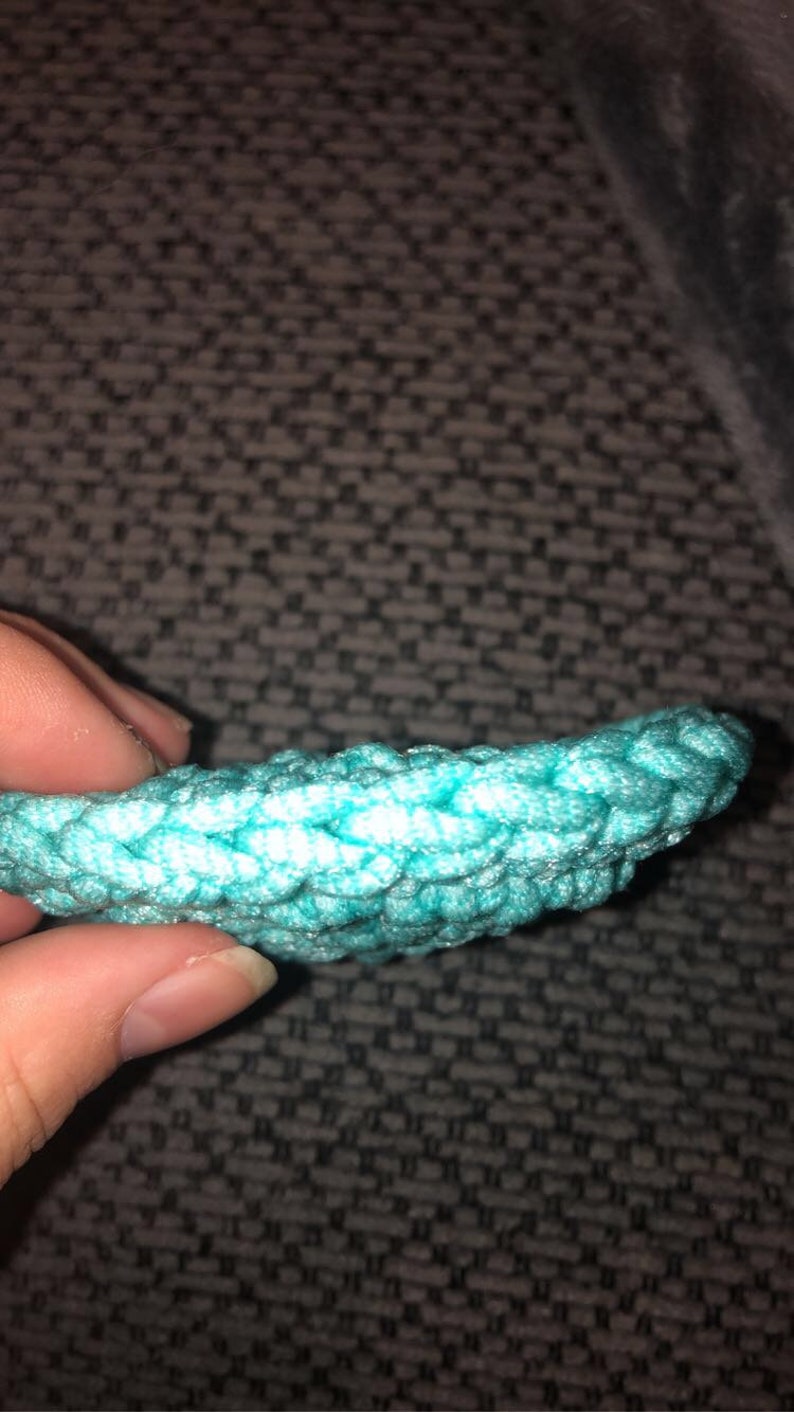 May include: Close-up of a turquoise crocheted item, possibly a decorative element or part of a larger craft project. The texture is clearly visible, with a tight, woven pattern. The color is a bright, vibrant turquoise.