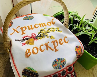 May include: White embroidered cloth with the text "Христос воскрес" (Christ is Risen) in Cyrillic script. The cloth is decorated with colourful beaded eggs and a sprig of pussy willow.