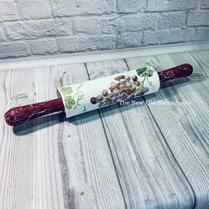 May include: A white rolling pin with a red handle and a grape design. The rolling pin is on a wooden surface. The text "The New Old Barakholka" is visible on the rolling pin.