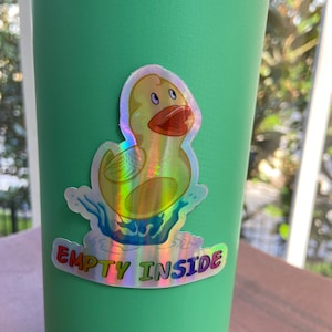 May include: A green reusable water bottle with a holographic sticker of a yellow rubber ducky in a pool of water. The sticker says "EMPTY INSIDE".